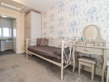 A bedroom with a metal daybed with cushions a grey dressing table with a mirror and a stool and a wardrobe