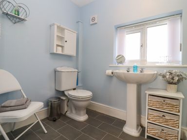 A bathroom with a toilet sink storage drawers and a folding chair at Mollys Bit Church Westcote near Bourton-On-The-Water