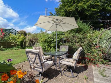 An outdoor patio area with a table, four cushioned chairs, and a large umbrella in a garden at Molly's Bit Church Westcote near Bourton-On-The-Water