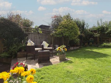 A garden with patio chairs and table near a wooden fence and various plants at Molly's Bit in Church Westcote near Bourton-On-The-Water