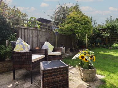A garden patio with two wicker chairs and a table near a sunflower planter at Mollys Bit in Church Westcote near Bourton On The Water