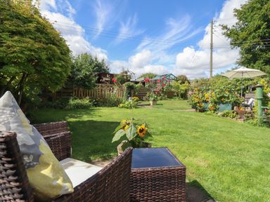 A garden with wicker chairs and cushions sunflowers and a parasol at Mollys Bit in Church Westcote near Bourton-On-The-Water