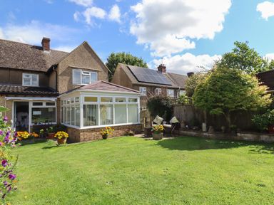 A backyard garden with green lawn flowers and a glass conservatory attached to a house at Molly's Bit in Church Westcote near Bourton-On-The-Water