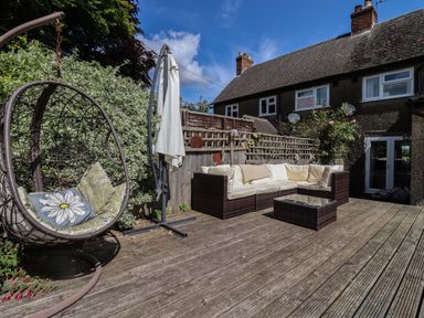 A wooden deck with outdoor seating and hanging chair outside a house at Molly's Bit in Church Westcote near Bourton-On-The-Water