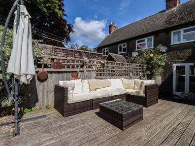 An outdoor patio with a wicker corner sofa with cushions a coffee table and a large umbrella near a wooden fence at Mollys Bit Church Westcote near Bourton-On-The-Water