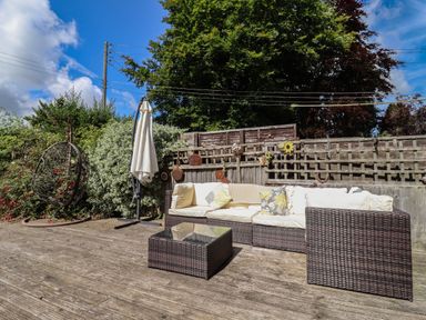 An outdoor patio with a wicker sofa set and a glass coffee table next to a hanging chair and umbrella at Molly's Bit Church Westcote near Bourton-On-The-Water