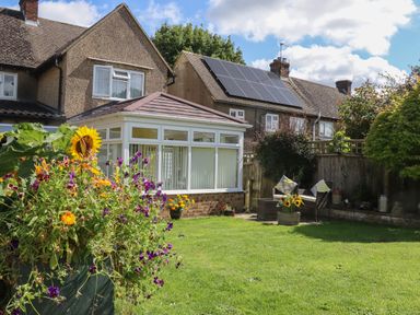 A garden with flowers and a lawn next to a house with a conservatory and solar panels on the roof at Molly's Bit in Church Westcote near Bourton-On-The-Water