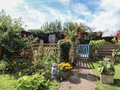 A garden with flowers shrubs a pathway a wooden fence and a blue gate at Molly's Bit Church Westcote near Bourton-On-The-Water