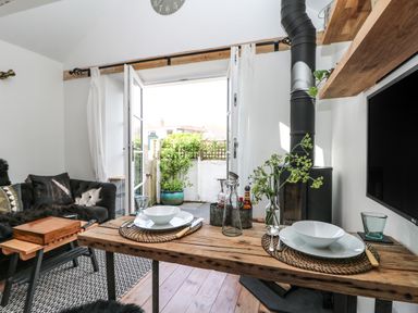 A dining table with plates and bowls in a living room with an open door leading outside at Rocket Cart House in Lizard