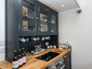 A kitchen counter with bottles mugs and glasses next to a stove at Rocket Cart House in Lizard