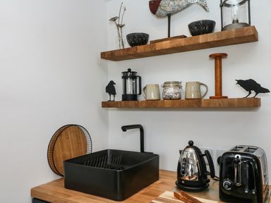 A kitchen countertop with a black sink a kettle toaster wooden shelves with mugs and decorative items at Rocket Cart House in Lizard