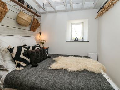 A bedroom with a bed with pillows and a blanket a small window and hanging baskets at Rocket Cart House in Lizard