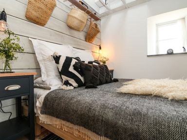 A bedroom with a bed with gray blankets pillows and side tables with hanging baskets on the wall at Rocket Cart House in Lizard