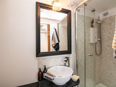 A bathroom with a round sink and faucet a mirror a glass shower enclosure and towels at Rocket Cart House in Lizard