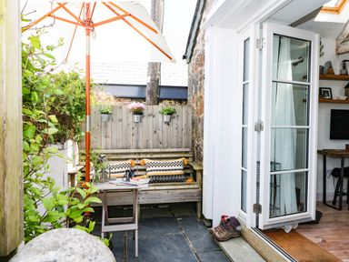 A small outdoor patio with a wooden bench table and umbrella next to an open glass door at Rocket Cart House in Lizard