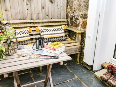 Outdoor seating area with wooden bench and table with books binoculars and lantern at Rocket Cart House in Lizard