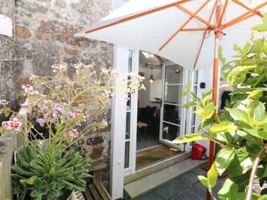 An outdoor patio area with plants a white open door and a large white umbrella at Rocket Cart House in Lizard