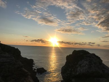 A sunset over the ocean with rocky cliffs on the sides at Rocket Cart House in Lizard