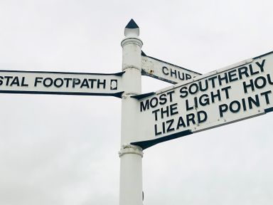 A white signpost with black text pointing to coastal footpath church and most southerly the light house lizard point at Rocket Cart House in Lizard