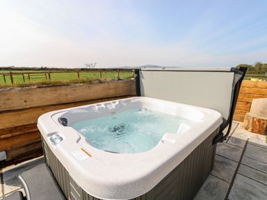 An outdoor hot tub with bubbling water on a stone patio next to a wooden fence with fields and hills in the background at Glowty Brynbedw in Efailwen