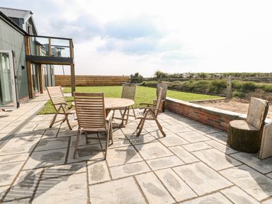 An outdoor patio with wooden chairs and table next to a grassy area at Glowty Brynbedw in Efailwen
