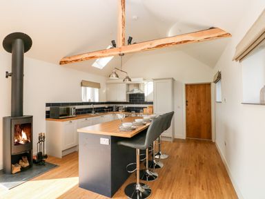 A kitchen with an island and bar stools a wood burning stove and exposed ceiling beams at Glowty Brynbedw in Efailwen