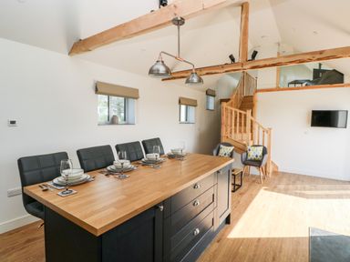 A dining area with a wooden table set for four beside a staircase and two chairs at Glowty Brynbedw in Efailwen