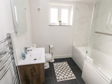 A bathroom with a sink and vanity unit toilet bathtub with glass shower screen and window with plant on sill at Glowty Brynbedw in Efailwen