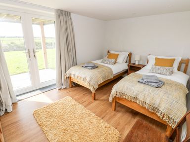 A bedroom with two single beds a nightstand between the beds a rug on the wooden floor and glass doors covered with curtains at Glowty Brynbedw in Efailwen