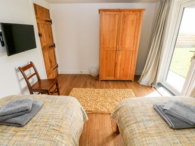 A bedroom with two beds and towels a wooden chair wooden wardrobe and a TV on the wall at Glowty Brynbedw in Efailwen
