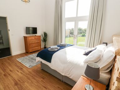 A bedroom with a bed pillows folded towels a wooden chest of drawers a flat screen TV a plant and double doors leading outside at Glowty Brynbedw in Efailwen