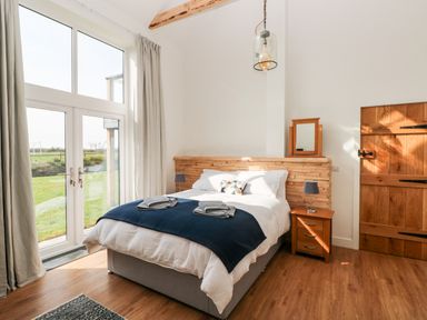A bedroom with a double bed a wooden headboard two bedside tables with lamps a wooden door and large windows with curtains at Glowty Brynbedw in Efailwen