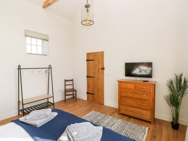 A bedroom with a bed with folded towels a wooden dresser with a tv a wooden chair a clothes rack and a potted plant at Glowty Brynbedw in Efailwen