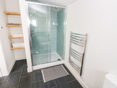 A bathroom with a glass shower enclosure tiled with green tiles shelves with towels and a chrome towel radiator at Glowty Brynbedw in Efailwen