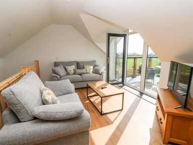 A seating area with two gray sofas a wooden coffee table a flat screen tv on a wooden stand and glass doors leading to a balcony at Glowty Brynbedw in Efailwen