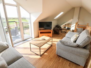 A living room with two sofas a coffee table a television and glass doors leading to a balcony at Glowty Brynbedw in Efailwen
