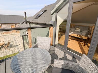 Balcony with a round table and two chairs overlooking a patio with wooden chairs and a round table at Glowty Brynbedw in Efailwen