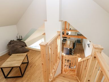 A wooden staircase leading down to a kitchen area with a dining table set with plates and chairs at Glowty Brynbedw in Efailwen