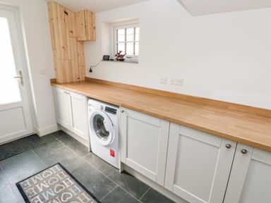 A utility room with washing machine under wooden countertop and white cabinets at Glowty Brynbedw in Efailwen