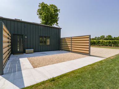 A modern exterior with a dark grey door and window beside a gravel area and tiled walkway at Tilia Barn in Wincanton