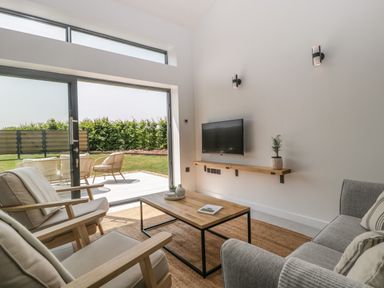 A living room with armchairs sofa coffee table and wall-mounted TV with glass door opening to garden at Tilia Barn in Wincanton