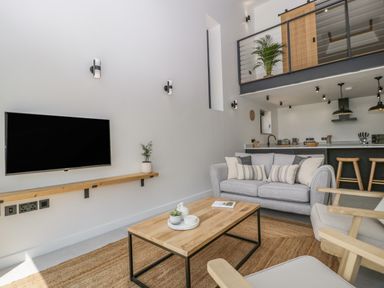 A living room with a sofa armchairs wooden coffee table and a wall-mounted television at Tilia Barn in Wincanton