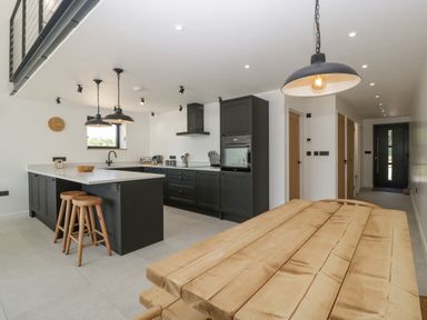 A kitchen with black cabinets a wooden dining table and stools at Tilia Barn in Wincanton