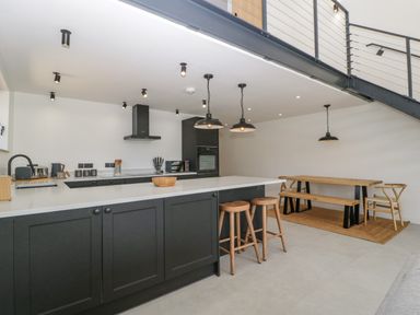 A kitchen with black cabinets and stools and a dining area with wooden table and bench at Tilia Barn in Wincanton