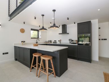 A modern kitchen with black cabinets white countertops two wooden stools and pendant lights at Tilia Barn in Wincanton