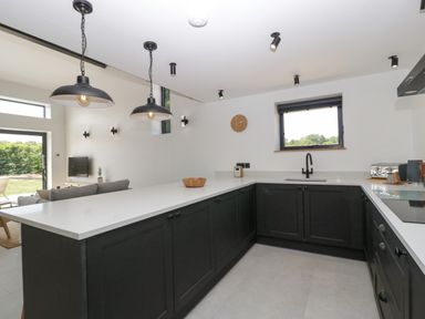 A kitchen with black cabinets white countertops black pendant lights and a window at Tilia Barn in Wincanton