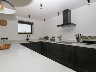 A kitchen with black cabinets white countertops a black faucet a stove a knife set and a window at Tilia Barn in Wincanton