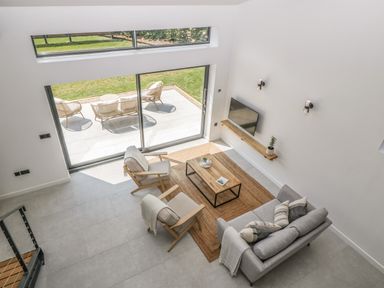 A living room with a sofa two armchairs a coffee table and a wall-mounted TV with patio doors leading to outdoor seating at Tilia Barn in Wincanton