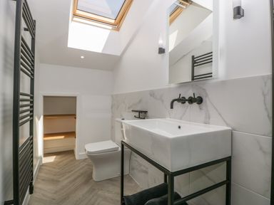 A bathroom with a white sink on a black metal stand a toilet a skylight and a black towel radiator at Tilia Barn in Wincanton