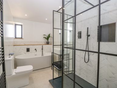 A bathroom with a bathtub toilet sink and a black framed glass shower at Tilia Barn in Wincanton